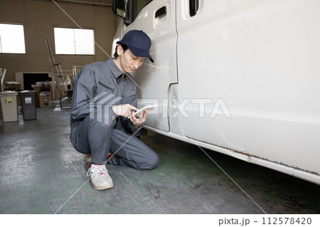 傷ついた車の修理の見積もりをする作業員 傷ついた車の修理の見積もりをする作業員 112578420