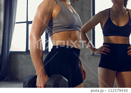 Cropped photo of young woman with athletic body in sportswear wet after productive weightlifting training at gym. Cropped photo of young woman with athletic body in sportswear wet after productive weightlifting training at gym. 112579430