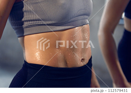 Close up of young woman with athletic body in sportswear wet after productive weightlifting training at gym. 112579431