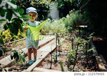 Adorable girl watering garden plants with watering can Adorable girl watering garden plants with watering can 112579483
