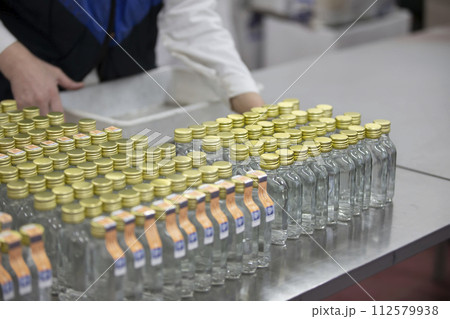 A row of glass bottles on a conveyor belt for the production of alcoholic beverages. 112579938