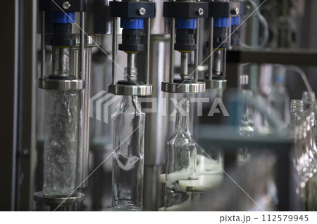 A long row of glass bottles on a conveyor belt. Production of alcoholic beverages. A long row of glass bottles on a conveyor belt. Production of alcoholic beverages. 112579945