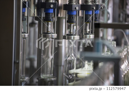 A long row of glass bottles on a conveyor belt. Production of alcoholic beverages. 112579947