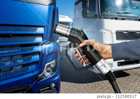 Hand with H2 fueling nozzle on a background of hydrogen fuel cell truck. Eco-friendly commercial vehicle concept.. Hand with H2 fueling nozzle on a background of hydrogen fuel cell truck. Eco-friendly commercial vehicle concept.. 112580517