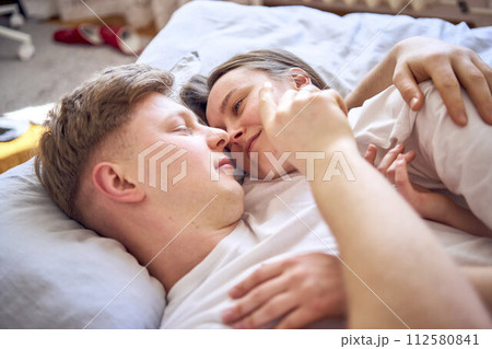 a young couple is lying on the bed, the girl is on the boy's shoulder, tender hugs 112580841