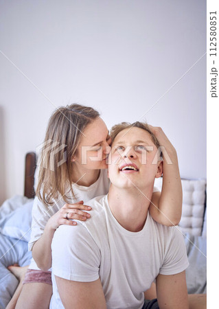a young couple on the bed, the woman plays and bites the boy's ear 112580851