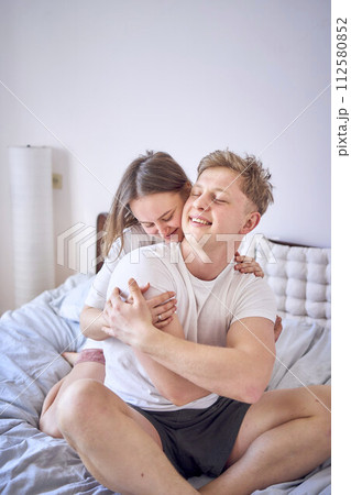 young couple on bed, woman hugs man from behind young couple on bed, woman hugs man from behind 112580852