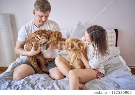 young couple spending time with their animals, a red cat and a cockapoo girl, playing and laughing young couple spending time with their animals, a red cat and a cockapoo girl, playing and laughing 112580909