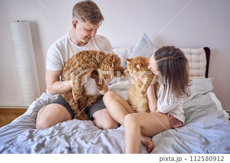 young couple spending time with their animals, a red cat and a cockapoo girl, playing and laughing 112580912