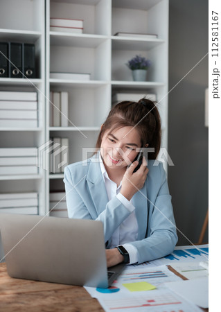 Happy Asian business women have the joy of talking on the smartphone, tablet, and laptop in the home office, Wearing a blue suite. 112581167