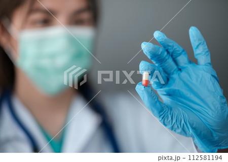 Female woman doctor holding up a pill vitamin supplement drug cure on grey background 112581194