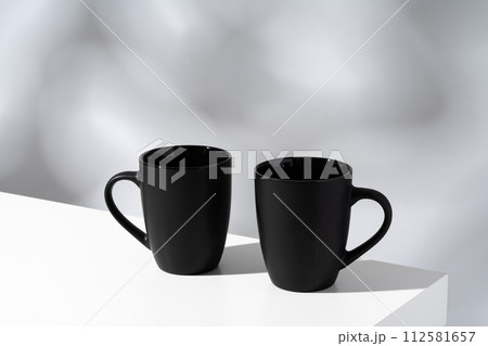Two black ceramic mugs on gray background with shadows Two black ceramic mugs on gray background with shadows 112581657