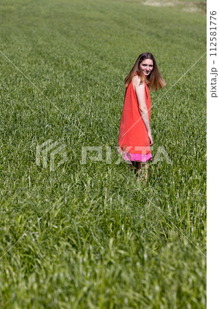 Joyful Woman in Vibrant Dress Standing in Lush Green Field Joyful Woman in Vibrant Dress Standing in Lush Green Field 112581776