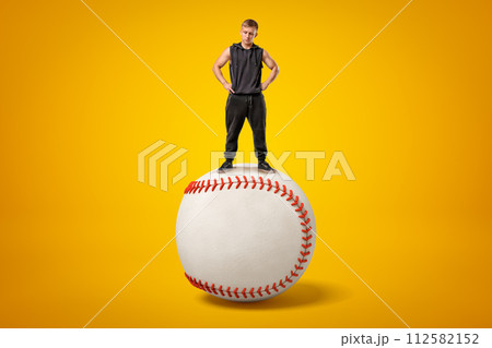 Strong muscular young man standing on big white baseball ball on yellow background 112582152