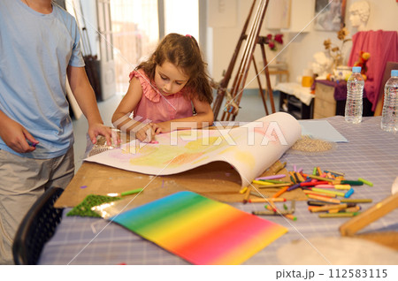 Talented inspired elementary age schoolgirl in pink dress, painting in the creative art school. 112583115