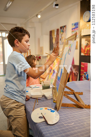 Talented primary school kids concentrate on acrylic color picture painting on canvas in art classroom. Visual art Talented primary school kids concentrate on acrylic color picture painting on canvas in art classroom. Visual art 112583198