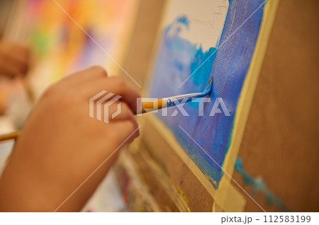 Close-up hand of a student holding paintbrush and painting picture on canvas in the art school. Close-up hand of a student holding paintbrush and painting picture on canvas in the art school. 112583199