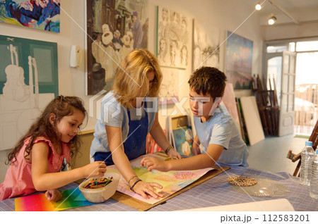 Painter teaches kids painting on canvas, shares advice and skills with learners during art-class in creative art studio Painter teaches kids painting on canvas, shares advice and skills with learners during art-class in creative art studio 112583201
