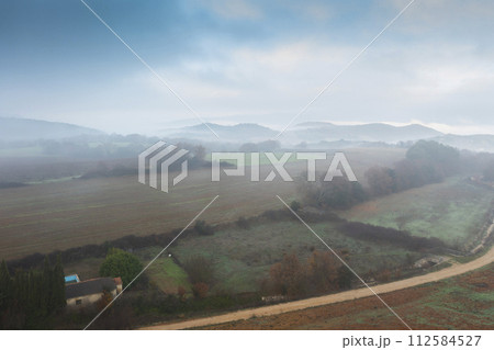 Aerial view of cultivated plots and hedges in autumn with fog. Aerial view of cultivated plots and hedges in autumn with fog. 112584527