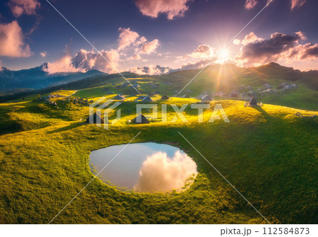 Aerial view of mountain village on green hills and pond at sunset Aerial view of mountain village on green hills and pond at sunset 112584873