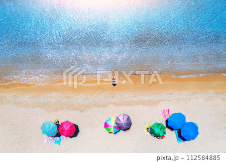 Aerial view of a woman on sandy beach, umbrellas and blue sea Aerial view of a woman on sandy beach, umbrellas and blue sea 112584885