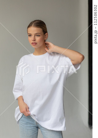 Beautiful blonde girl in a white oversized T-shirt and blue jeans posing on a gray background 112586302
