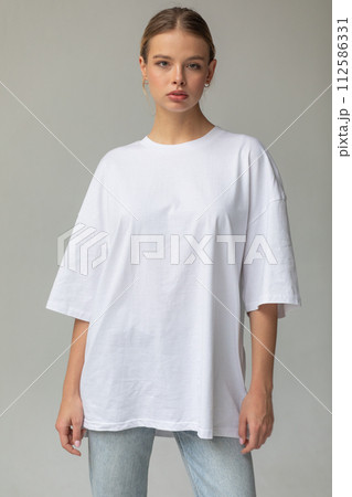 Beautiful blonde girl in a white oversized T-shirt and blue jeans posing on a gray background 112586331