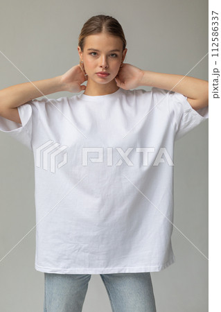 Beautiful blonde girl in a white oversized T-shirt and blue jeans posing on a gray background 112586337