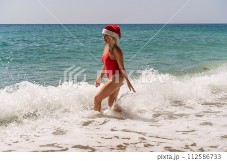A woman in Santa hat on the seashore, dressed in a red swimsuit. New Year's celebration in a hot country 112586733