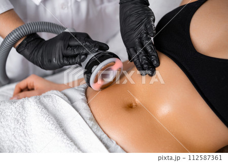 Close cosmetologist using ultrasound device while performing lifting procedure on woman belly. 112587361