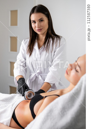 Portrait of a beautician doing body sculpting by ultrasonication procedure to a young woman. Portrait of a beautician doing body sculpting by ultrasonication procedure to a young woman. 112587380