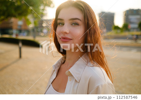 Mysterious red haired girl stands in the park at sunset.  112587546
