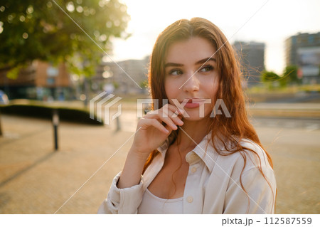 Mysterious red haired girl stands in the park at sunset. Mysterious red haired girl stands in the park at sunset. 112587559