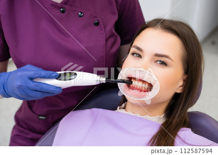 Doctor dentist fixes a filling in teeth using UV lamp to a beautiful patient. Doctor dentist fixes a filling in teeth using UV lamp to a beautiful patient. 112587594