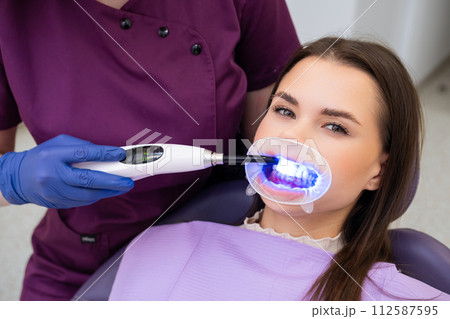 Dentist employs a UV lamp to cure the fillings in the patients teeth. Dentist employs a UV lamp to cure the fillings in the patients teeth. 112587595