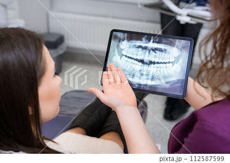 Utilizing a tablet to showcase the X ray image, the female dentist discusses treatment strategies with the patien Utilizing a tablet to showcase the X ray image, the female dentist discusses treatment strategies with the patien 112587599