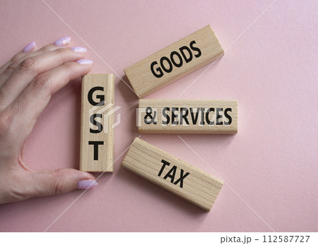GST - Goods and Services Tax symbol. Concept word GST on wooden blocks. Businessman hand. Beautiful pink background. Business and GST concept. Copy space. 112587727