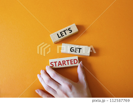 Lets get started symbol. Concept words Lets get started on wooden blocks. Beautiful orange background. Businessman hand. Business and Lets get started concept. Copy space. 112587769
