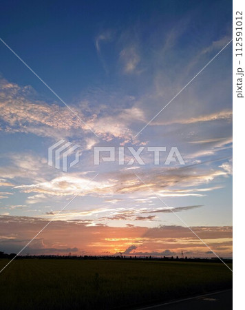 地平線に沈む夕日のオレンジ色に染まる夏の空と雲 112591012