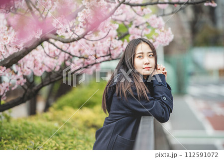 桜の下で手すりに手をかけている女子高生 112591072