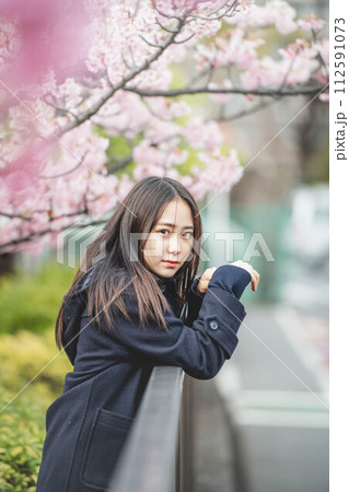 桜の下で手すりに手をかけている女子高生 112591073
