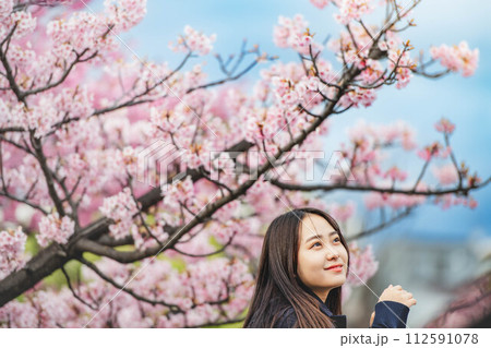 桜の下で手すりに手をかけている女子高生 112591078