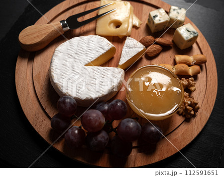 Sliced Brie cheese served with knife, honey, nuts and grape on wooden board Sliced Brie cheese served with knife, honey, nuts and grape on wooden board 112591651
