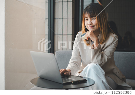 Young woman holding credit card and using laptop computer. Businesswoman working at home. Online shopping, e-commerce, internet banking, spending money, working from home concept 112592396