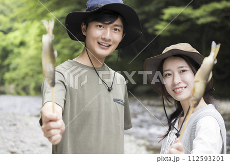 キャンプ場で鮎の塩焼きを食べるカップル 112593201