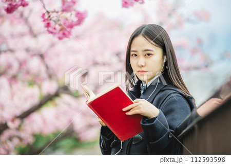 満開の桜の下で音楽を聴きながら勉強をする女子高校生 112593598