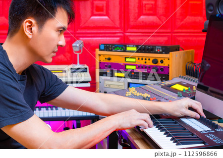 asian handsome professional music producer arranging a hit song on computer by midi keyboard in home studio asian handsome professional music producer arranging a hit song on computer by midi keyboard in home studio 112596866