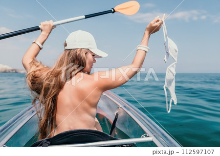 Woman in kayak back view. Happy young woman with long hair floating in transparent kayak on the crystal clear sea. Summer holiday vacation and cheerful female people relaxing having fun on the boat Woman in kayak back view. Happy young woman with long hair floating in transparent kayak on the crystal clear sea. Summer holiday vacation and cheerful female people relaxing having fun on the boat 112597107