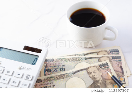 福沢諭吉の肖像の一万円紙幣と電卓、ペン、淹れたてのコーヒーが入ったコーヒーカップ 福沢諭吉の肖像の一万円紙幣と電卓、ペン、淹れたてのコーヒーが入ったコーヒーカップ 112597507