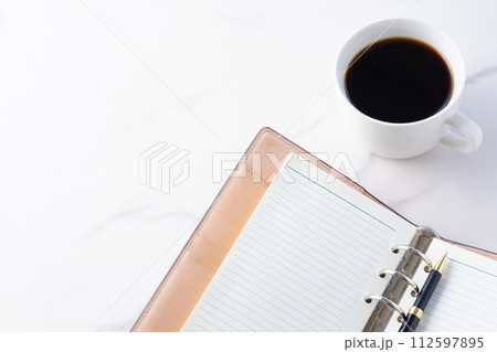 淹れたてのコーヒーを飲みながら、リング式のシステム手帳を開いてデスクワークをしているイメージ 112597895